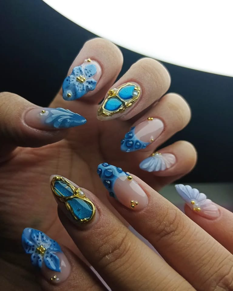 Nail art azul con flores, dorado y pedrería sobre uñas almendra