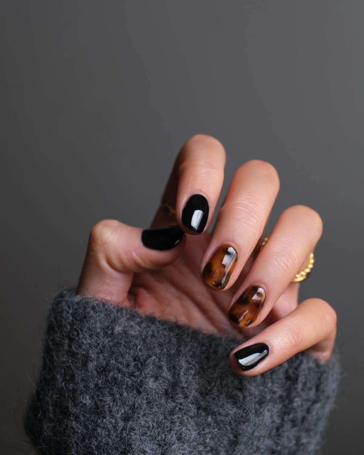 Manos con nail art de autor en tonos café y dorado sobre un suéter tejido