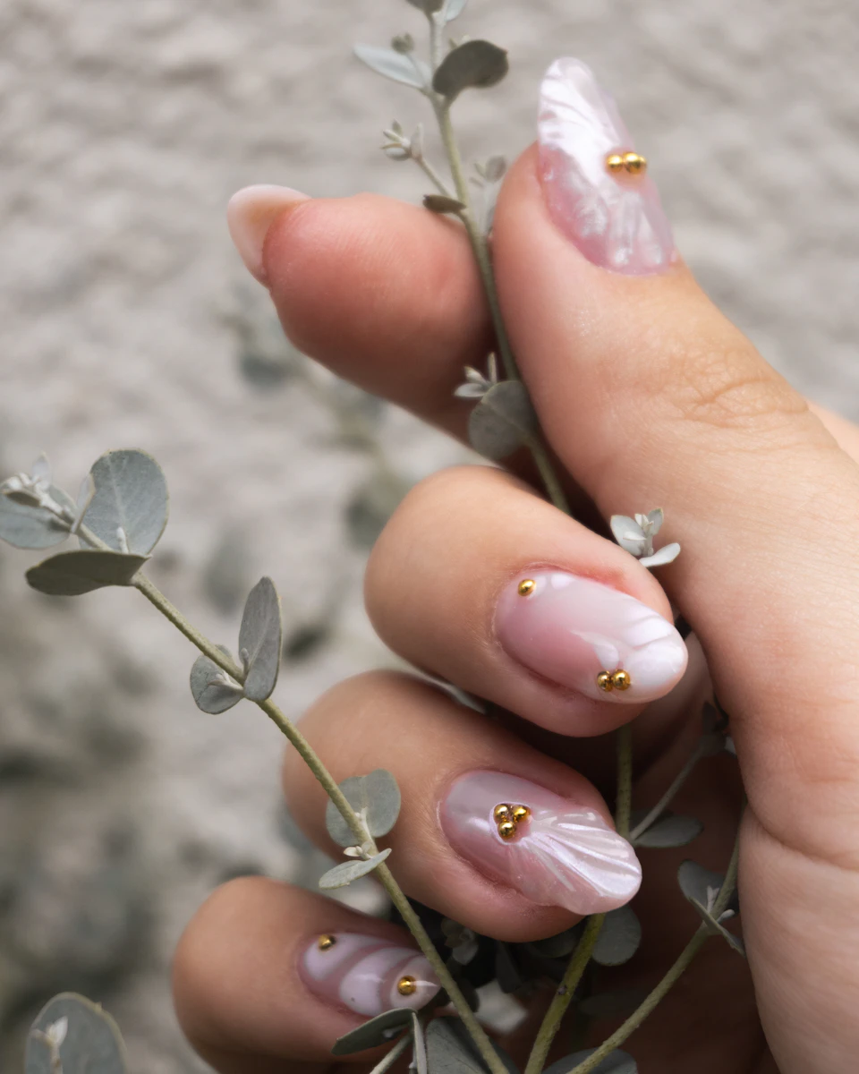 Uñas con arte floral fino y detalles dorados sosteniendo una rama de eucalipto
