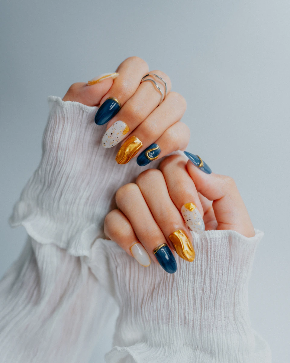 Nail art ornamentado en azul marino, dorado y blanco sobre tejido de gasa