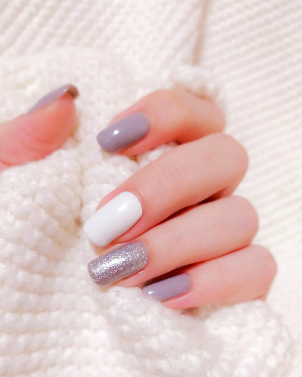 Manicura en blanco y malva con acento de glitter plateado sobre tejido crema