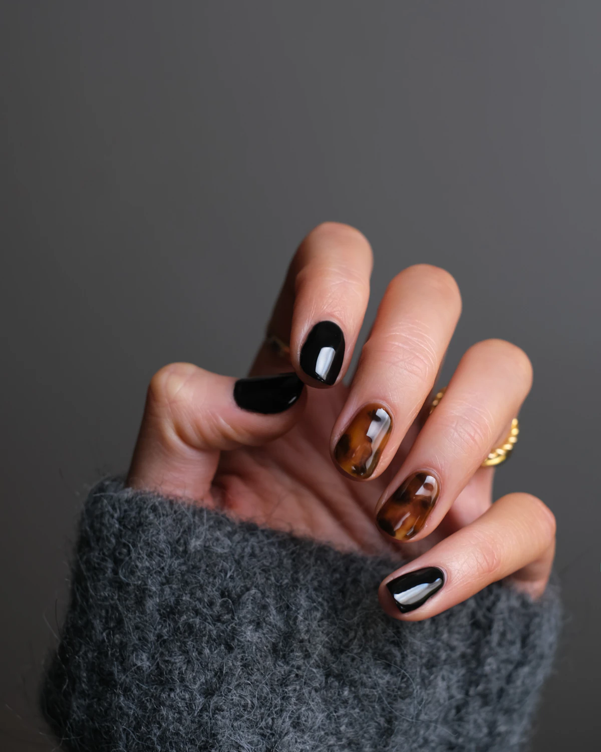 Manos con nail art de autor en tonos café y dorado sobre un suéter tejido